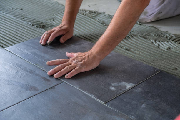 Worker's hands pressing ceramic floor tiles laid on applied adhesive